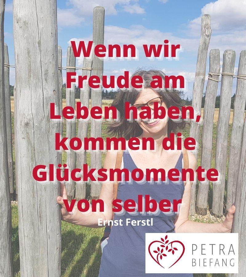Strahlende Frau öffnet Holztor mit Zitat: Wenn wir Freude im Leben haben, kommen die Glücksmomente von selber - Inspiration für mehr Lebensfreude, Selbstannahme und erfülltes Leben mit Petra Biefang