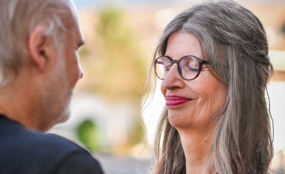 Petra Biefang und ihr Partner stehen gegenüber mit Hand auf das Herz des Gegenübers. Beide spüren ihre Liebe zueinander. Symbolik für Intimität, Nähe und Liebe