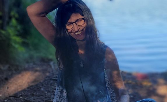 Lächelnde Frau mit langen Haaren am Seeufer, umgeben von Natur - Symbol für Selbstliebe, Weiblichkeit und Freiheit im Frauenheilkreis Pfaffenhofen.