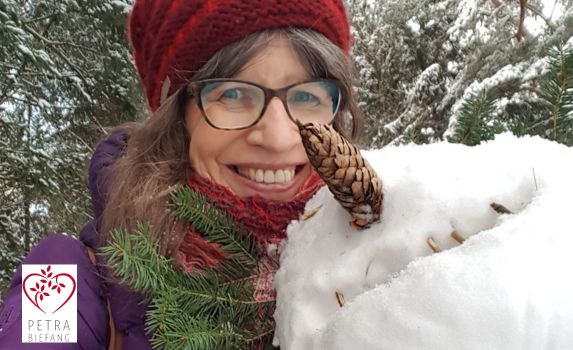 Lächelnde Frau im Schnee mit Tannenzweig und Zapfen - Winterlicher Frauenkreis mit Heilpraktikerin/ Psychotherapie in Pfaffenhofen