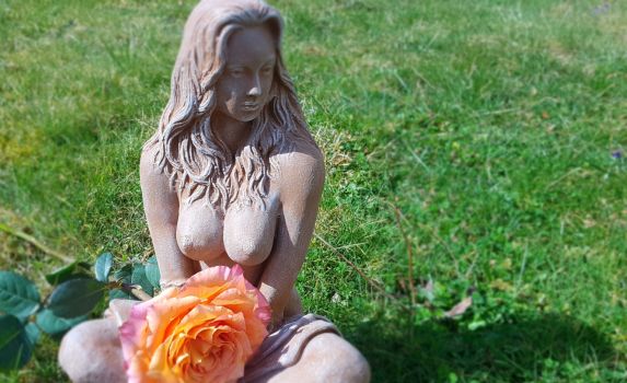 Frauenstatue auf Wiese mit orangefarbener Rose - Symbol für Weiblichkeit, Kraft und Erdverbundenheit