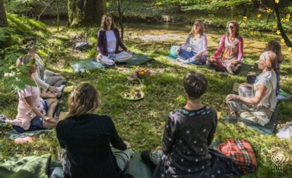Frauen sitzen im Kreis auf einer Wiese im Wald, Blumen in der Mitte. Symbol für Schwesternschaft, Gemeinschaft, Meditation und Weiblichkeit. Einladung zum Frauenkreis in Pfaffenhofen .
